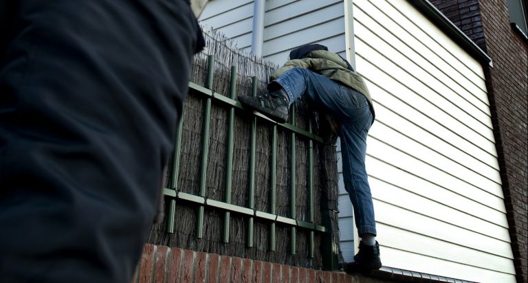 Foto van inbreker die huis probeert binnen te dringen door over een hek te klimmen.