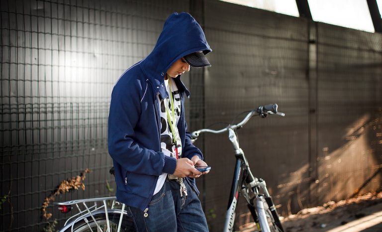 Op de foto is een jongen met een fiets te zien. Hij is verdiept in zijn smartphone.