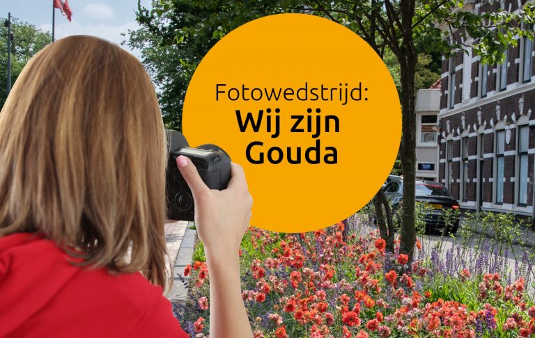 Op de foto ziet u een vrouw die een foto maakt in Gouda. Op de foto staat ook de naam van de fotowedstrijd. De naam van de wedstrijd is ´Wij zijn Gouda´.