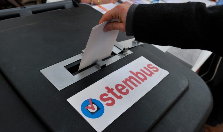 Stembus waar een hand een stembiljet ingooit.