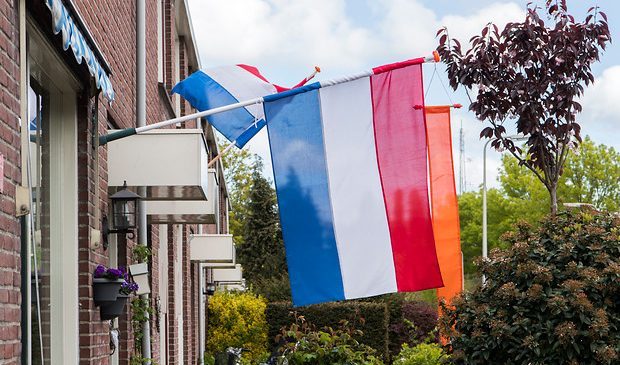 De Nederlandse vlag met een oranje wimpel hangt uit bij een woonhuis.