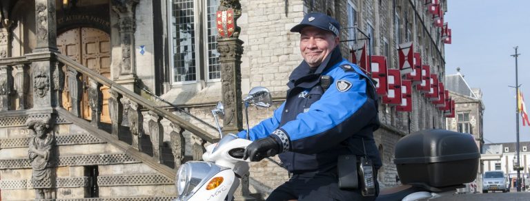 Op de foto poseert wijkboa Johan in uniform met een scooter van Stadstoezicht op de Markt in Gouda.