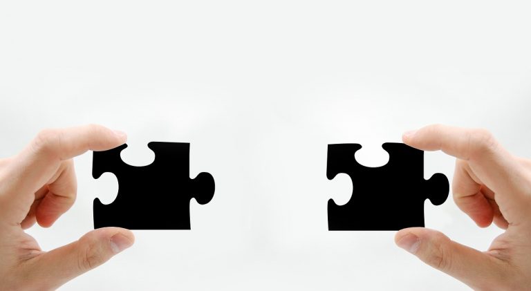 twee handen houden zwarte puzzelstukjes vast die in elkaar passen.