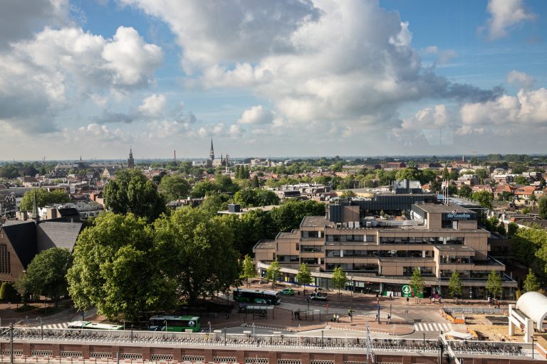 Een foto van het uitzicht vanaf het Huis van de Stad. De bovenste helft van de foto is een blauwe lucht met wolken, onderin het uitzicht op het station en de rest van de binnenstad.