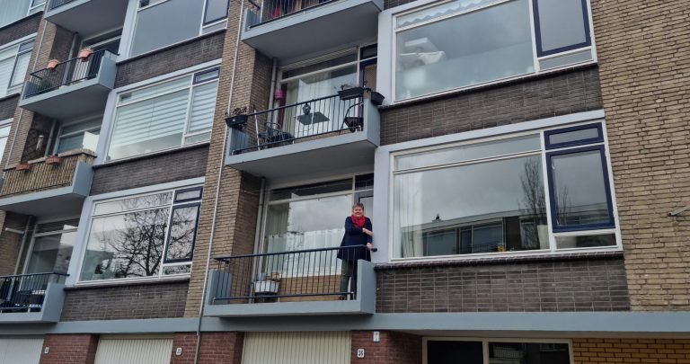 Een portiekflat, met uitzicht op meerdere ramen van verschillende appartementen. Ester Broug staat op haar balkon.