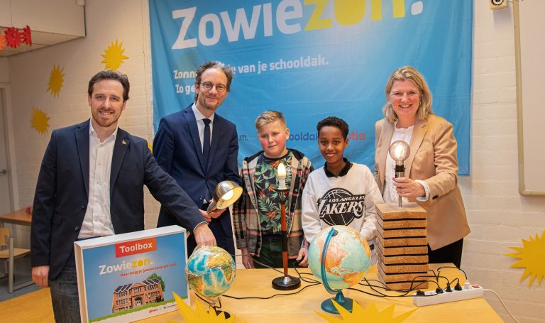 Wethouders Thierry van Vugt en Michel klijmij - van der laan met twee kinderen en Selina Tuhrer van Eneco met een poster van Zowiezon op de achtergrond en op de tafel voor hun twee aardbollen en houten modellen en lampjes.