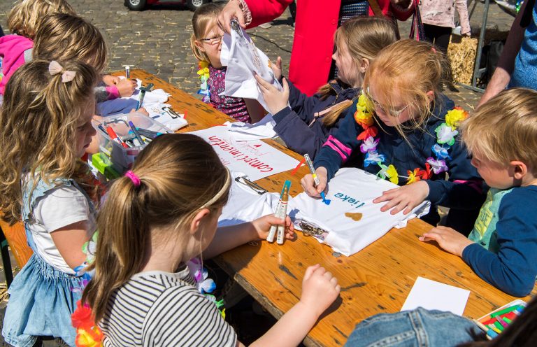 Kinderen kleuren en schrijven op t-shirts op de Markt.