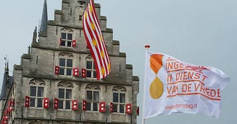 Stadhuis op de Markt en de vlag van de veteranendag met de tekst 'ingezet in dienst van de vrede'.