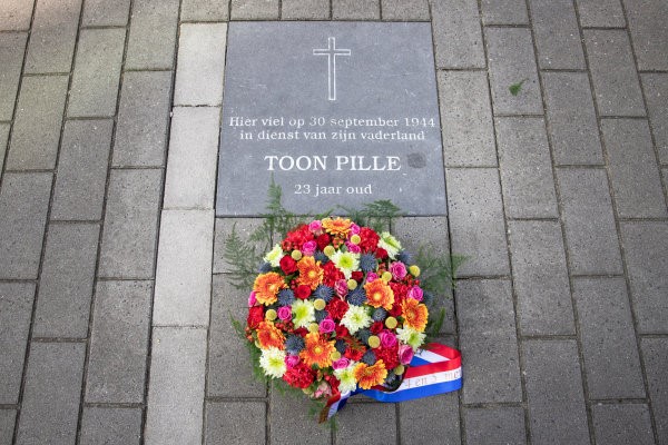 Foto van de herdenkingsteen van Toon Pille voor het Huis van de Stad met een bloemen krans.