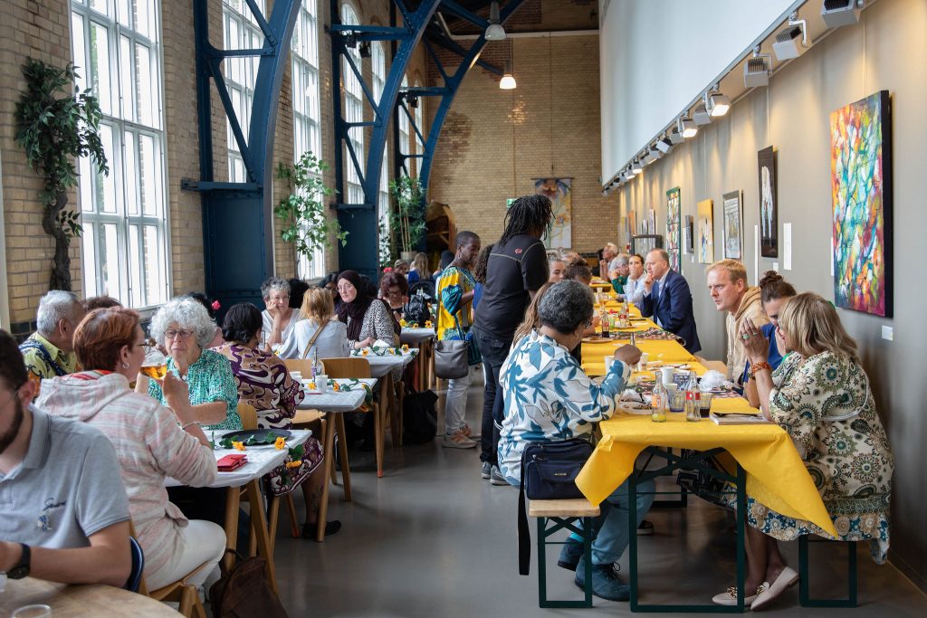 De foto is genomen in de Garenspinnerij tijdens de gezamenlijke maaltijd. Mensen zitten samen aan tafel en eten.