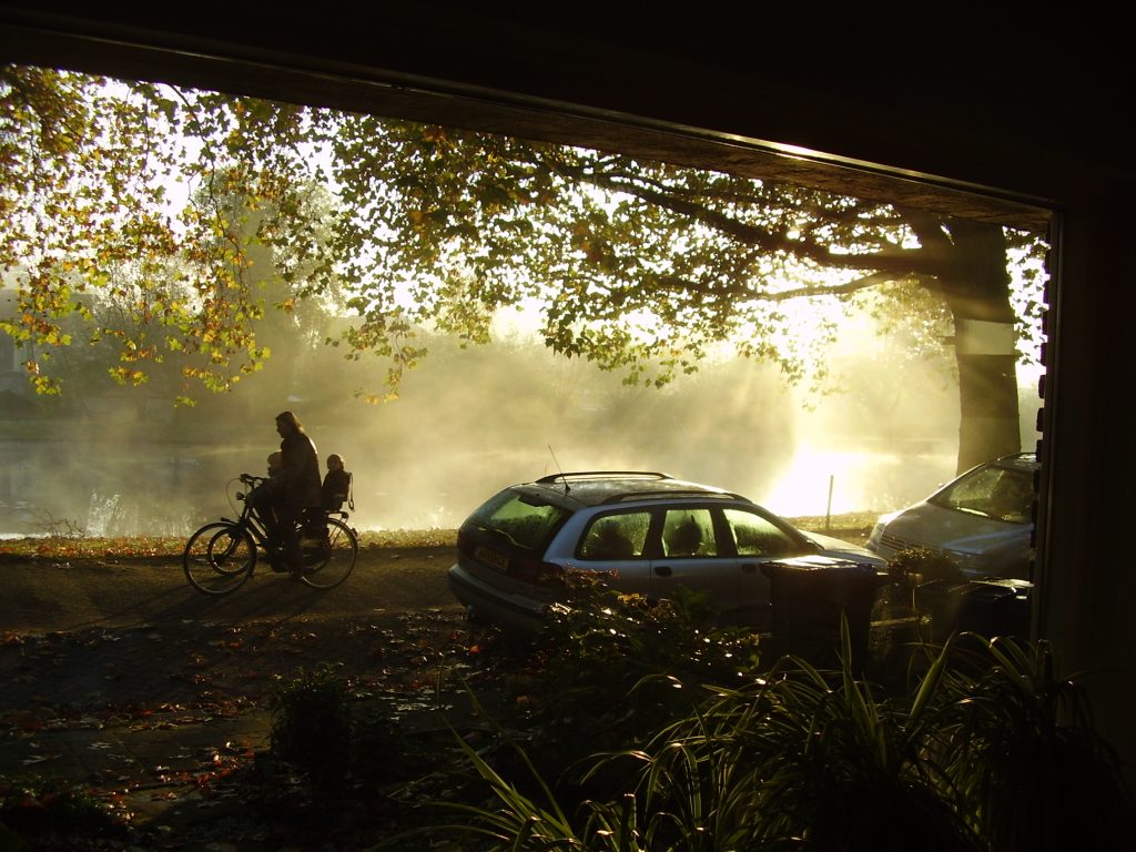 Foto van een persoon die fietst langs de gracht tijdens zonsopkomst met mist.