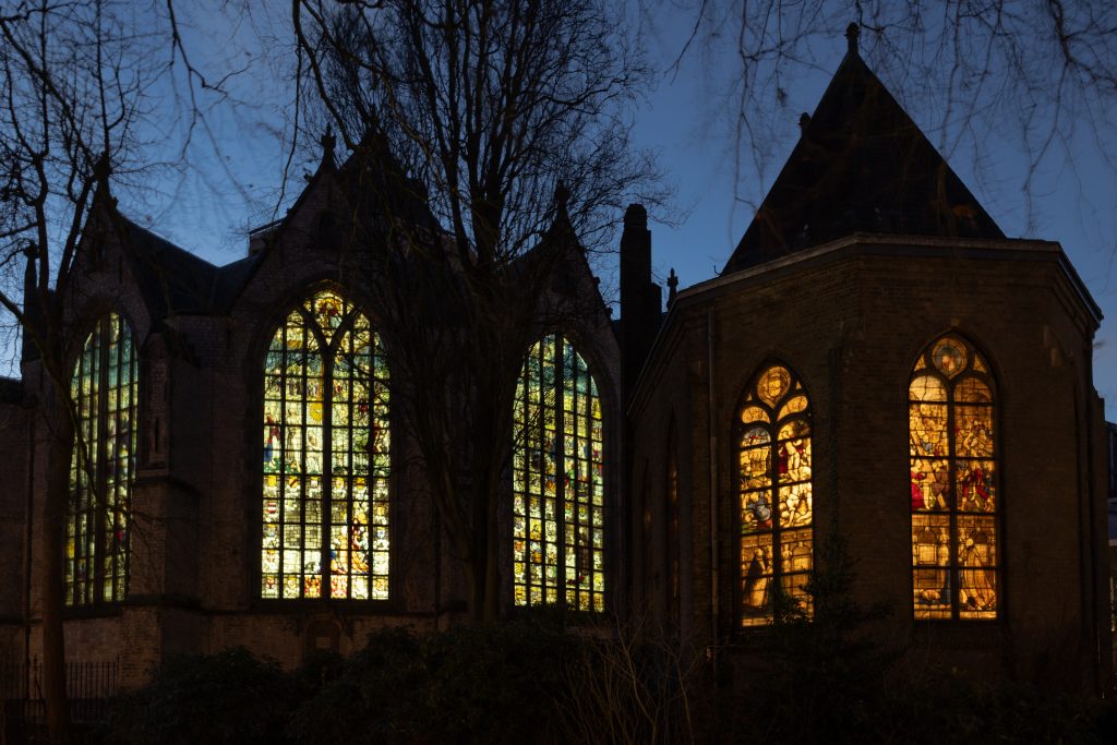 Foto van de Sint-Janskerk in het donker waarbij er licht achter de ramen schijnt