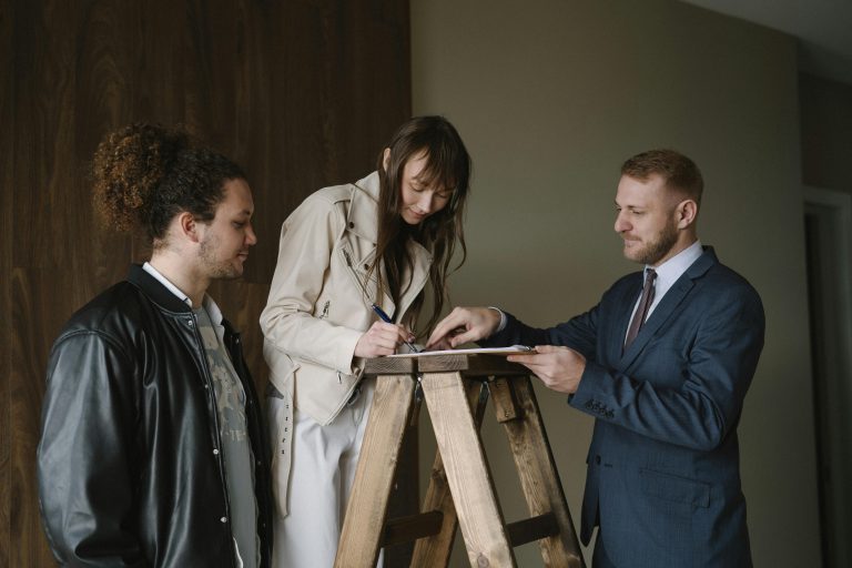 Een man en een vrouw tekenen een document met een makelaar erbij.