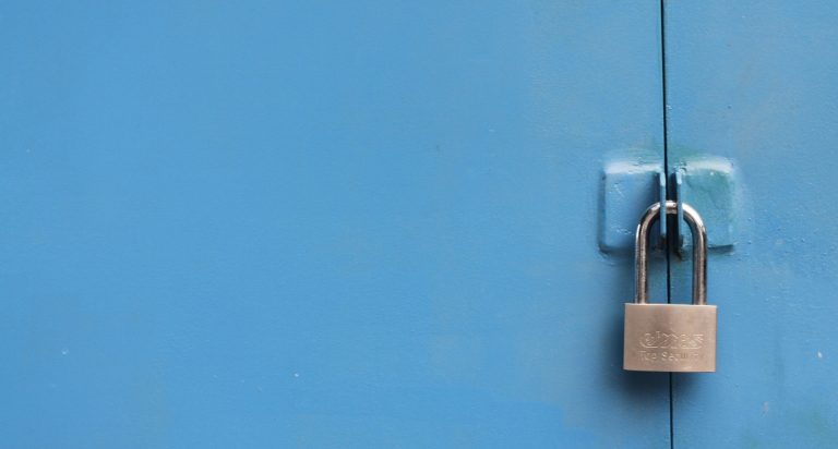 Op de foto is een blauwe deur te zien die op slot zit met een hangslot.