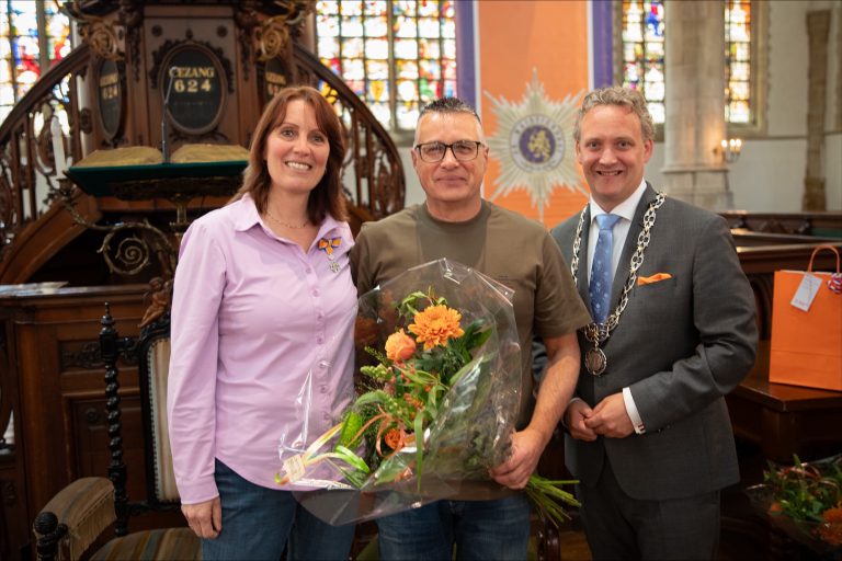 Linda Verschut poseert met haar lintje. Naast haar staan een man en burgemeester Pieter Verhoeve.