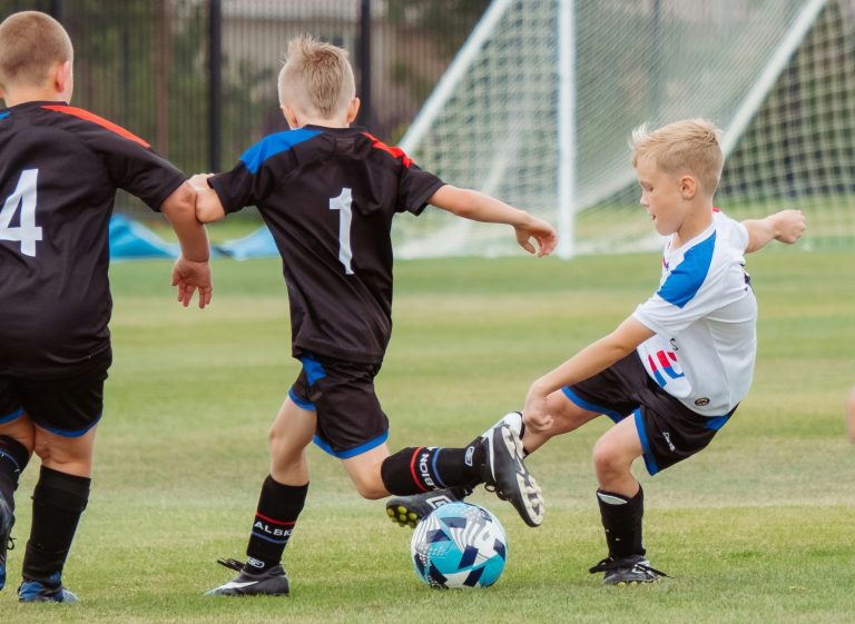 Op de foto zijn voetballende kinderen op een voetbalveld te zien.