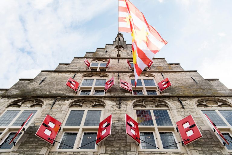 Foto van het stadhuis met wapperende vlag, van onderaf genomen.