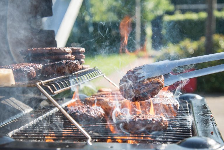 Een barbecue die gebruikt wordt. Op de barbecue ligt vlee. Er komt veel rook vanaf.