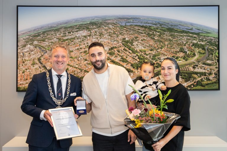 Mouad neemt op de foto samen met zijn vrouw Laila en kind de heldenpenning in ontvangst. Uitgereikt door Burgemeester Pieter Verhoeve.