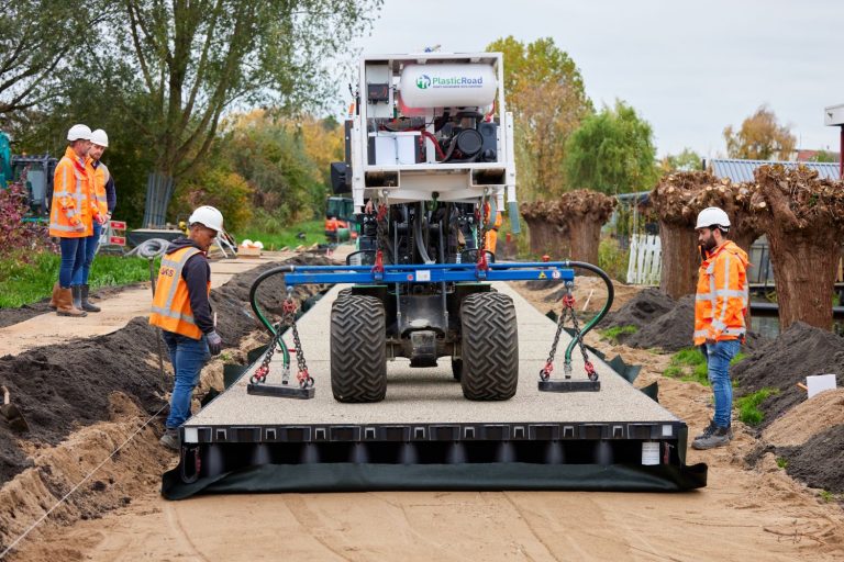 Foto van wegwerkzaamheden met vier mannen die de plastic road aanleggen met een machine.