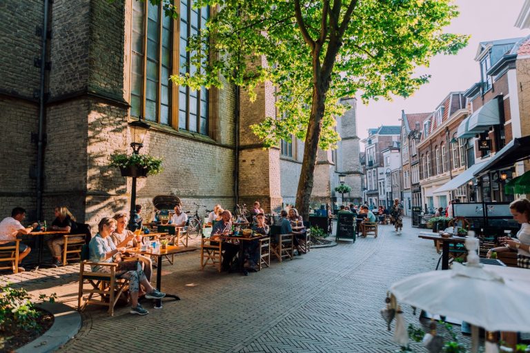Aan een straat in Gouda zitten mensen aan verschillende tafeltjes bij elkaar.
