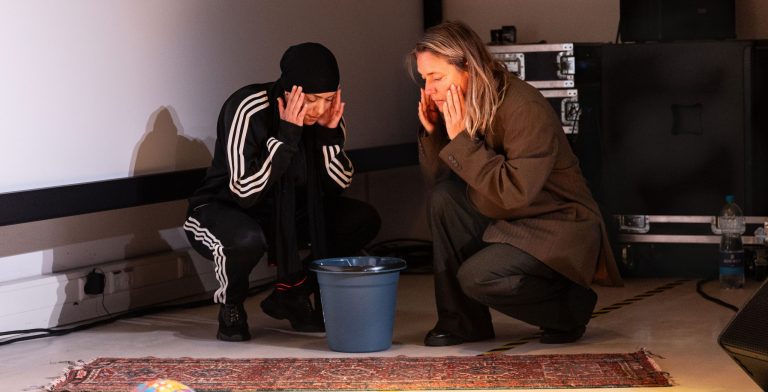 2 vrouwen zitten met hun handen voor hun gezicht op de grond.