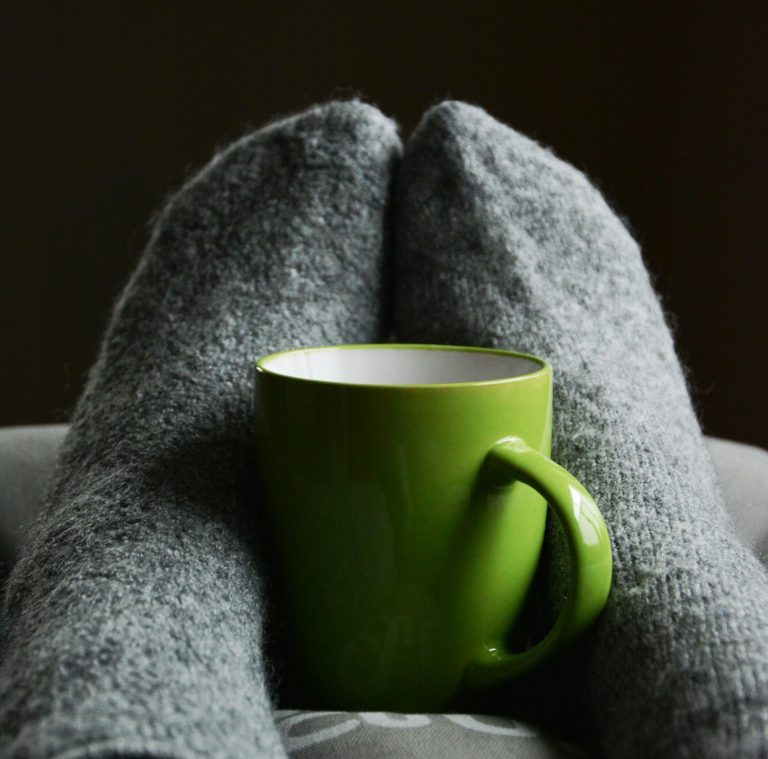 2 voeten met dikke sokken. Tussen de voeten in staat een kopje.