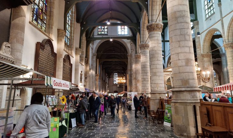 De duurzame markt in de Sint-Janskerk. Er staan kraampjes en er lopen mensen langs de kraampjes