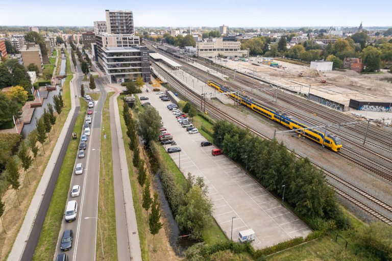 Op de foto staat het gebied van de spoorzone. De trein en station gouda, het gebied waar parkeerplekken zijn, en de Burgemeester Jamessingel.