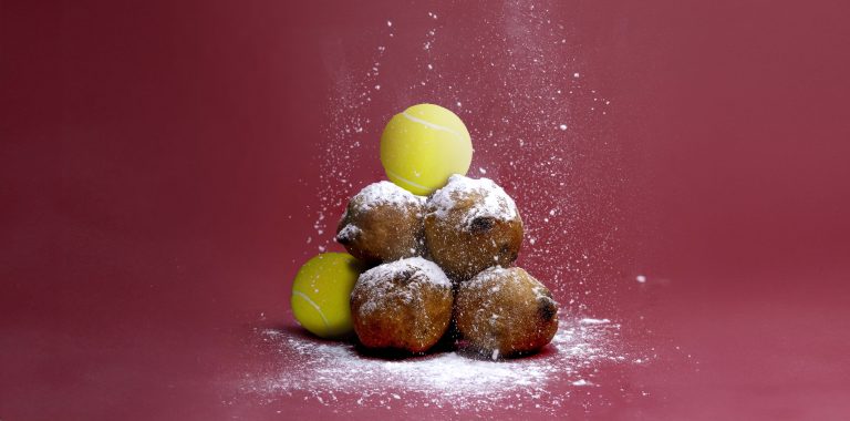 een stapeltje oliebollen en tennisballen. Er wordt suikerpoeder overheen gestrooid.