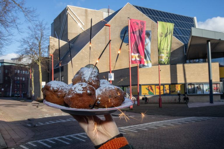 iemand houdt een bord met oliebollen vast. In de oliebollen staan siervuurwerk sterretjes gestoken.