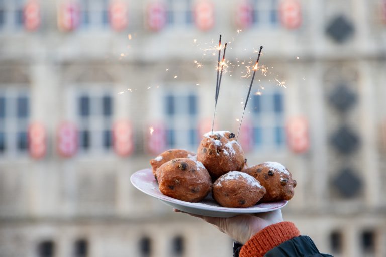 Iemand houdt een bord met oliebollen omhoog. In de oliebollen steken sterretjes.
