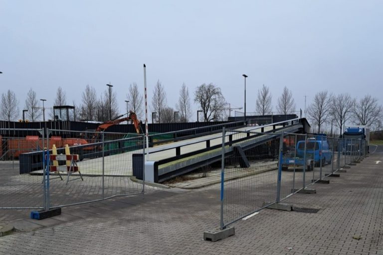 Een foto van de oprit van het Ecopark in Gouda. Om de oprit staan hekken, omdat deze wordt hersteld.