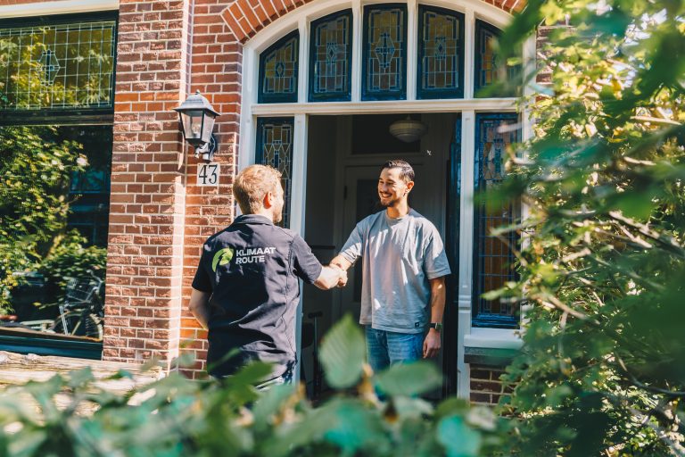Een adviseur van Klimaatroute schudt aan de deur de hand van een blije bewoner.