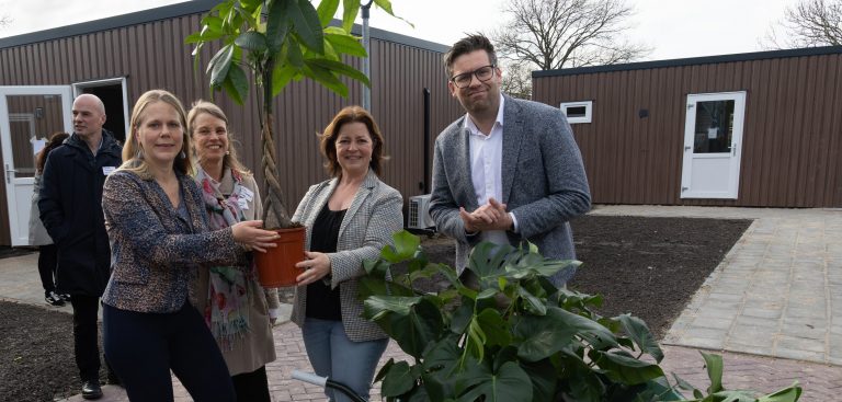 Op de foto staan wethouders Anna van Popering-Kalkman en Jan Kees Oppelaar samen met directeur-bestuurder Anne ter Steege van Mozaïek Wonen en Christine Eskes, directeur Zorg van het Leger des Heils. Voor hen staat een kruiwagen met planten. Anna van Poepring overhandigt een plant aan Christine Eskes.