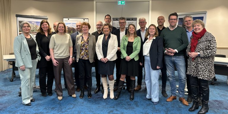 De samenwerking is vastgelegd in een intentieverklaring die vandaag is ondertekend. De deelnemende gemeenten zijn Gouda, Krimpenerwaard, Bodegraven-Reeuwijk, Waddinxveen en Zuidplas. De woningcorporaties die meedoen zijn Mozaïek Wonen, Woonpartners Midden-Holland, Woonbron, Stedelink, Groen Wonen Vlist en Qua Wonen. De vertegenwoordigers van deze organisaties staan samen met wethouder Oppelaar op deze foto.