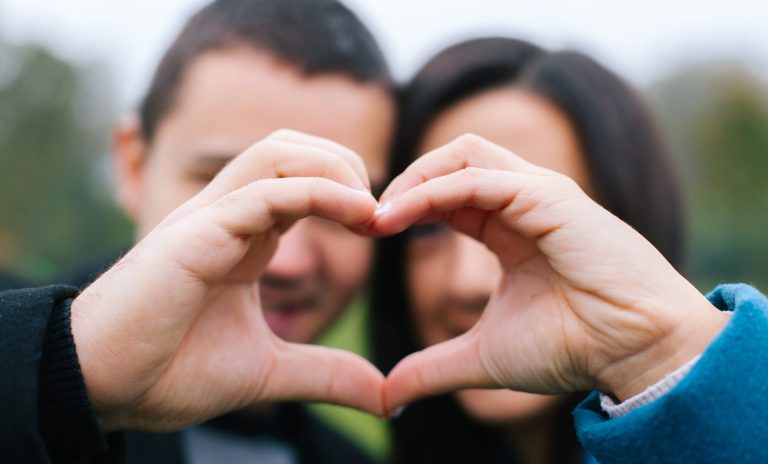 Een foto van een man en een vrouw die samen met hun handen een hartje vormen.